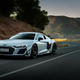 a grey 2023 audi r8 gt seen from the front as it accelerates around a curve of a winding mountain road at dusk